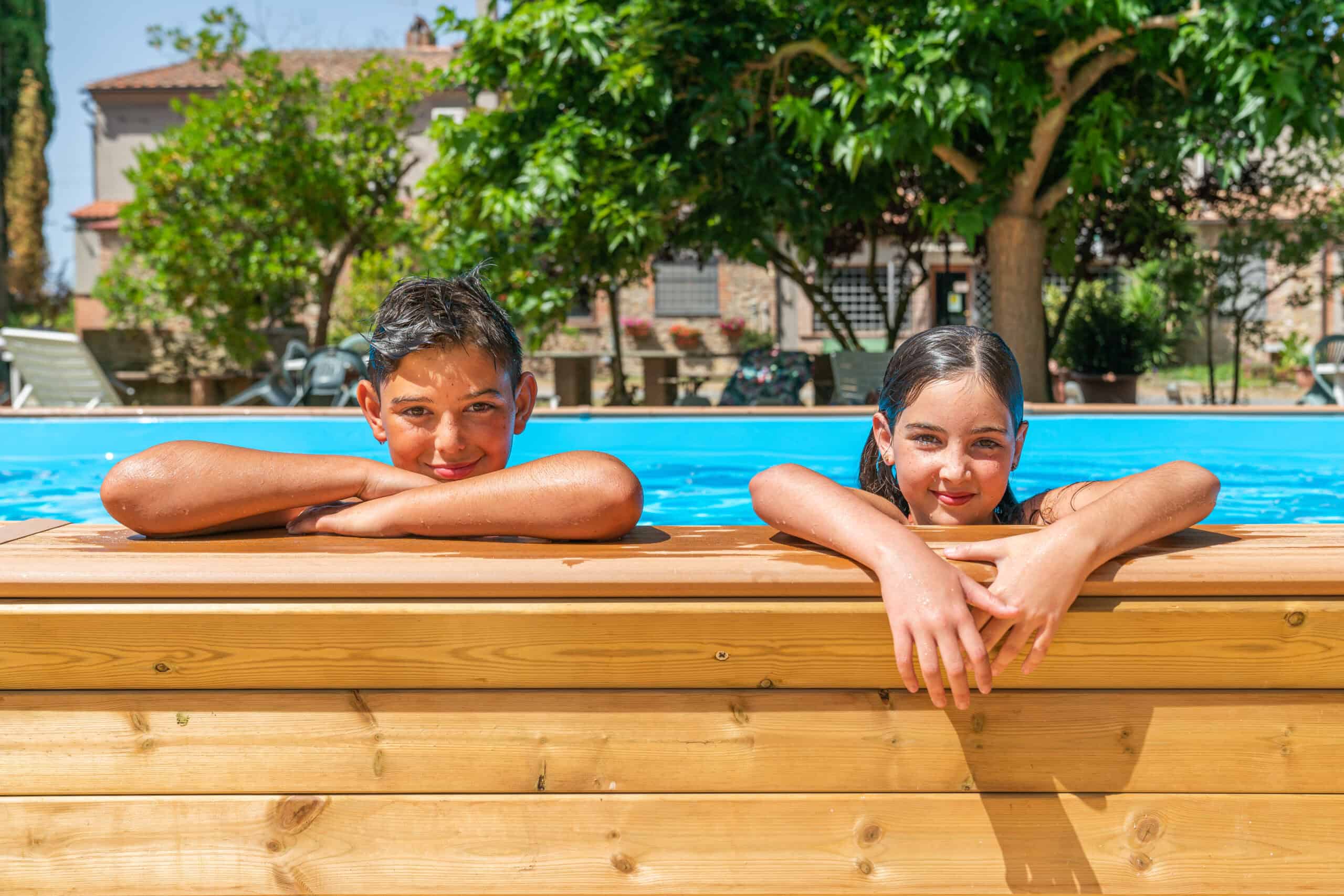 Bambini che si rilassano a bordo piscina in legno, in un contesto naturale e familiare.